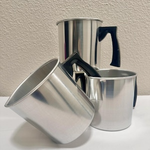 Peut inclure: Trois mugs en aluminium argenté avec des poignées noires. Les mugs sont empilés les uns sur les autres.