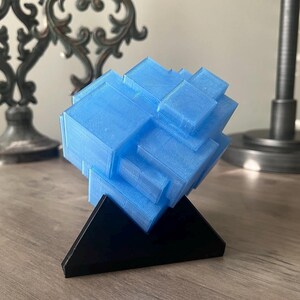 Puede incluir: Una escultura geom&eacute;trica azul impresa en 3D sobre una base triangular negra.
