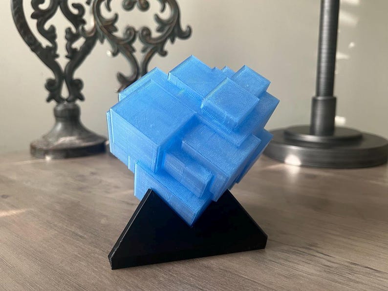 Puede incluir: Una escultura geom&eacute;trica azul impresa en 3D sobre una base triangular negra.
