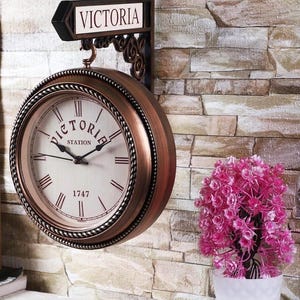 May include: A copper-colored double-sided clock with Roman numerals and a black metal sign that reads "VICTORIA STATION 1747".