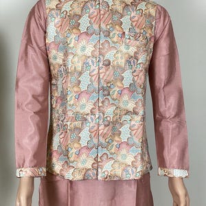 May include: A three-piece ensemble featuring a dusty rose kurta and pants, complemented by a patterned vest. The vest showcases a floral design in shades of pink, blue, and beige. The outfit is displayed on a mannequin.