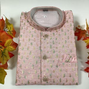 May include: A pink button-up shirt with a floral pattern and a small pocket on the left side. The shirt has a mandarin collar and a size tag that says "38".