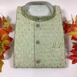 Pode incluir: Uma camisa verde estampada para homem com colarinho mandarim e fecho de bot&otilde;es. A camisa tem um bolso do lado direito e &eacute; decorada com bot&otilde;es dourados.