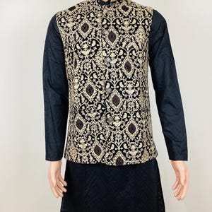 May include: A black and gold embroidered vest with a mandarin collar, worn over a black long-sleeved shirt and black bottoms. The vest features an ornate, repeating pattern in gold thread.