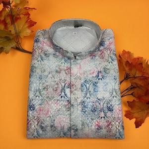 Puede incluir: Una camisa blanca de manga larga con cuello mandarín y estampado paisley colorido. La camisa tiene una etiqueta de talla que dice "38".