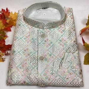 May include: A white embroidered jacket with a mandarin collar, featuring a geometric and floral pattern in pastel colors. The jacket has decorative buttons and a pocket. The size tag reads "44".