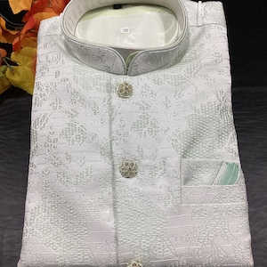 May include: White button-up shirt with a mandarin collar and a floral pattern. The shirt has three decorative buttons and a pocket on the right side. The size tag says "38".