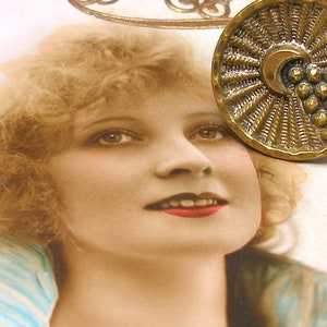 Puede incluir: Un botón vintage de latón con un diseño de rayos de sol y una luna creciente con un grupo de puntos en relieve. El botón está sobre un fondo blanco con una foto de una mujer.