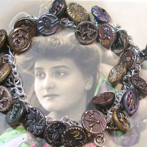 Puede incluir: Un brazalete de cadena de plata con una variedad de botones vintage en diferentes colores, formas y diseños. Los botones son de metal y tienen un aspecto desgastado y antiguo.