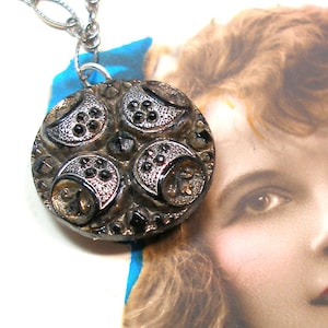 May include: A silver chain necklace with a black glass button pendant. The button has a raised design of four silver circles with black dots.