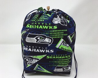 Puede incluir: Una bolsa de cordón azul con un patrón de Seattle Seahawks. La bolsa presenta el logotipo del equipo, las palabras "Seattle Seahawks" y un esquema de color verde y blanco.