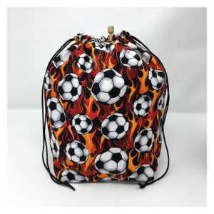 May include: A drawstring bag with a black and white soccer ball pattern on a red and orange flame background.