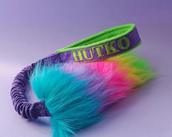 May include: A colorful, rainbow-colored, fluffy dog toy with a purple and green strap. The strap has the name "HUTKO" embroidered on it in green.