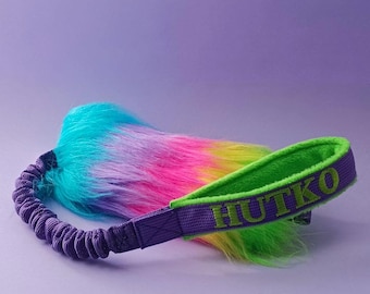 May include: A purple and green dog toy with a rainbow fur tail and the word "HUTKO" embroidered on the strap.