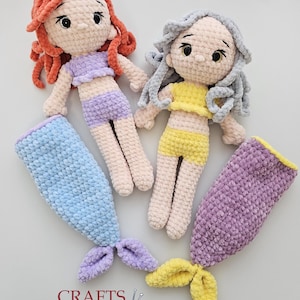 May include: Two handmade crochet mermaid dolls with red and grey hair, wearing tops and shorts. Each doll has a matching mermaid tail in blue, purple, and yellow. The image includes the text "Crafts by Lindar".