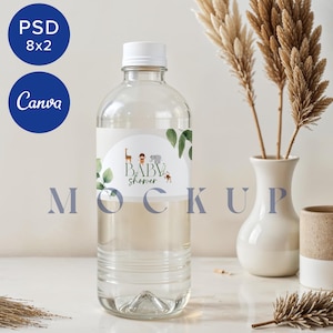 Puede incluir: Una botella de agua de plástico transparente con una etiqueta blanca que dice "Baby Shower" y presenta un tema de animales de la selva. La botella está sobre una superficie blanca con un jarrón de hierba de la pampa seca y una taza de cerámica pequeña.