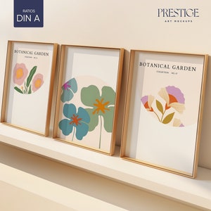 Puede incluir: Tres impresiones enmarcadas en dorado con fondos blancos e ilustraciones florales de colores. Las impresiones se titulan "Jardín Botánico" y están dispuestas en un estante blanco.