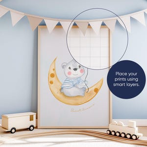 May include: A watercolor illustration of a gray bear wearing a blue and white striped shirt sitting on a yellow crescent moon. The text "Sweet Dreams" is written below the bear. The illustration is framed and hanging on a light blue wall.