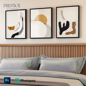 May include: Three abstract art prints with black frames hanging on a white wall above a bed with a wooden headboard and gray bedding.