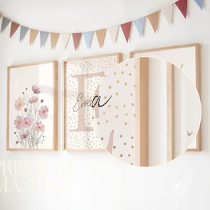 May include: Three framed prints with a white background. The print on the left features a watercolor illustration of pink flowers. The center print has a gold background with white polka dots and the letter "E" with the name "Ema" written in black. The print on the right is blank.