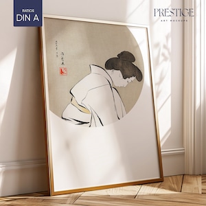 May include: A framed print of a black and white illustration of a woman in traditional Japanese clothing. The woman is standing in a circle with a red stamp in the corner. The print is in a gold frame and is leaning against a white wall.