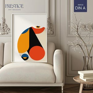 Puede incluir: Una impresión artística abstracta enmarcada con un diseño geométrico en formas naranja, amarillo, negro y azul. La obra de arte se exhibe sobre un sofá crema. El texto "PRESTIGE ART MOCKUPS" es visible. El marco es blanco.