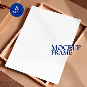 Puede incluir: Una hoja de papel blanca dentro de un marco de madera, con el texto "MOCKUP FRAME" en azul. Una caja de regalo marrón con una cinta está en la esquina superior izquierda. Un círculo azul con el texto "A SIZE" está en el centro superior.