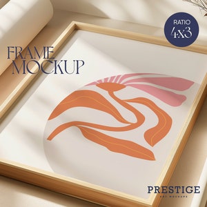 May include: A framed print with a 4x3 ratio featuring an abstract design of pink and orange shapes on a white background. The frame is made of natural wood and has a light brown finish. The text "FRAME MOCKUP" is visible in the top left corner of the image. The text "PRESTIGE ART MOCKUPS" is visible in the bottom right corner of the image.