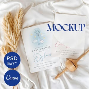 Op de afbeelding: Een mockup van een babyshower-uitnodiging met een blauw, wit en geel kleurenschema. De uitnodiging toont een cartoon-heteluchtballon met een baby erin. De tekst op de uitnodiging luidt: "Kom gezellig met ons mee naar een babyshower ter ere van Dylan". De uitnodiging ligt op een wit oppervlak met een droogbloemenarrangement en een houten speelgoed.
