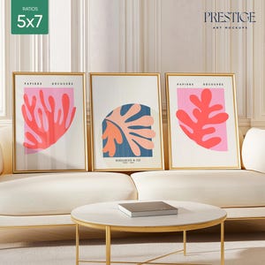 May include: Three framed art prints with abstract designs in pink, red, and coral colors. The prints are in gold frames and are hanging on a white wall above a white sofa.