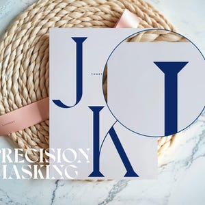 May include: A white card with the navy blue letters "J" and "K" and the word "TOGETHER" in small navy blue letters. The words "PRECISION MASKING" are printed in white at the bottom. The card is on a woven mat with a pink ribbon.