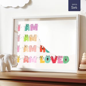 Pode incluir: Uma impressão emoldurada branca com as palavras "I AM LOVED" em letras coloridas com rostos de desenhos animados. As letras são empilhadas em forma de pirâmide.