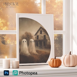 May include: A framed illustration of a spooky house with two white ghosts in front of it. The house is set against a backdrop of autumn foliage. The frame is on a table with two white candles and two pumpkins.
