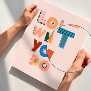 May include: A pink poster with the words "LOVE WHAT YOU DO" in colorful, playful typography. The letters are in various colors, including orange, blue, green, and pink. The poster is held by two hands.