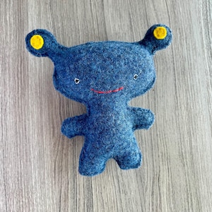 May include: A blue felt toy with yellow ears and a red smile. The toy has a simple, cartoon-like design.