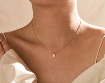 May include: A delicate gold chain necklace with a small oval-shaped pendant featuring a white stone.
