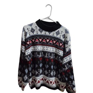 May include: A long-sleeve knit sweater featuring a mock neck and a repeating pattern of hearts, diamonds, and geometric shapes in black, white, red, and grey. The garment has a ribbed collar, cuffs, and hem, with a consistent fair isle style design.
