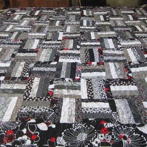 May include: A handmade quilt with a patchwork design in shades of black, white, and gray. The quilt features a variety of patterns, including floral prints and solid colors. The border has a black background with white and red floral designs.