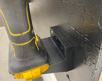 May include: A black wall mount with a yellow and black cordless drill attached to it.