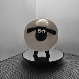 May include: Black and white sheep toilet paper holder with a white roll of toilet paper. The holder is on a black base with a mirrored surface.