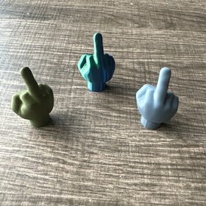 Puede incluir: Tres pequeñas figuritas de dedo medio impresas en 3D. Una es verde, otra es azul y otra es azul claro.