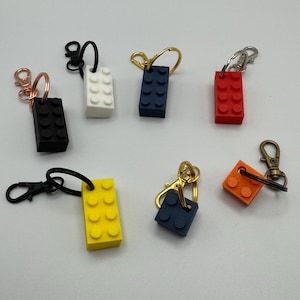 May include: A selection of brick-shaped keyrings in various colours. The keyrings are in black, white, blue, red, yellow, and orange. Each keyring has a metal ring or clasp for attaching keys.