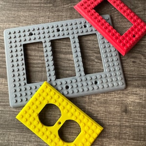 以下が含まれることがあります： グレー、赤、黄色の3Dプリントされたライトスイッチとコンセントカバー3つ。カバーはレゴブロックのように見えるように設計されています。