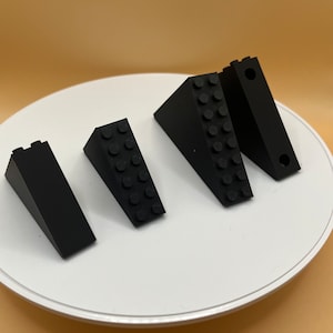 Könnte beinhalten: Vier schwarze Plastikbausteine in Keilform. Die Blöcke sind in einer Reihe auf einer weißen Oberfläche angeordnet.