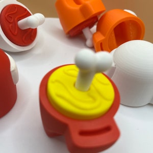 Peut inclure: Un ensemble de figurines de personnages Among Us rouges et oranges avec des os blancs. Les figurines sont en plastique et ont un aspect imprimé en 3D.