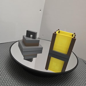 May include: A yellow and brown Minecraft-themed block with a gray and brown block on a black circular mirror surface.