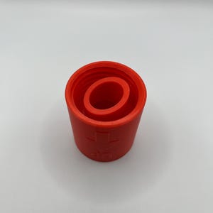 Può includere: Un tappo per bottiglia in plastica arancione brillante con un design a coste e un simbolo di freccia verso il basso. Il tappo è progettato per adattarsi a un'apertura di bottiglia standard.