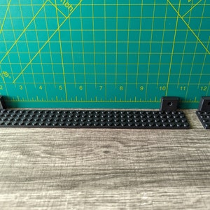 May include: Three black Lego pieces, two are small and one is long and rectangular. The long piece has a row of studs on one side.