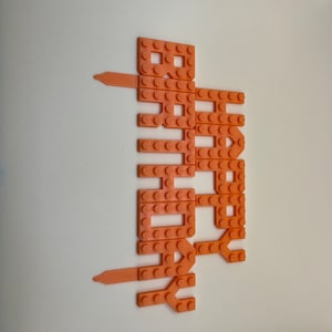 Orange 3D-printed plastic 'Happy Birthday' cake topper with a building-block brick texture design.