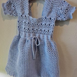 May include: A light blue crocheted dress with a square neckline, short sleeves, and a tie at the waist.